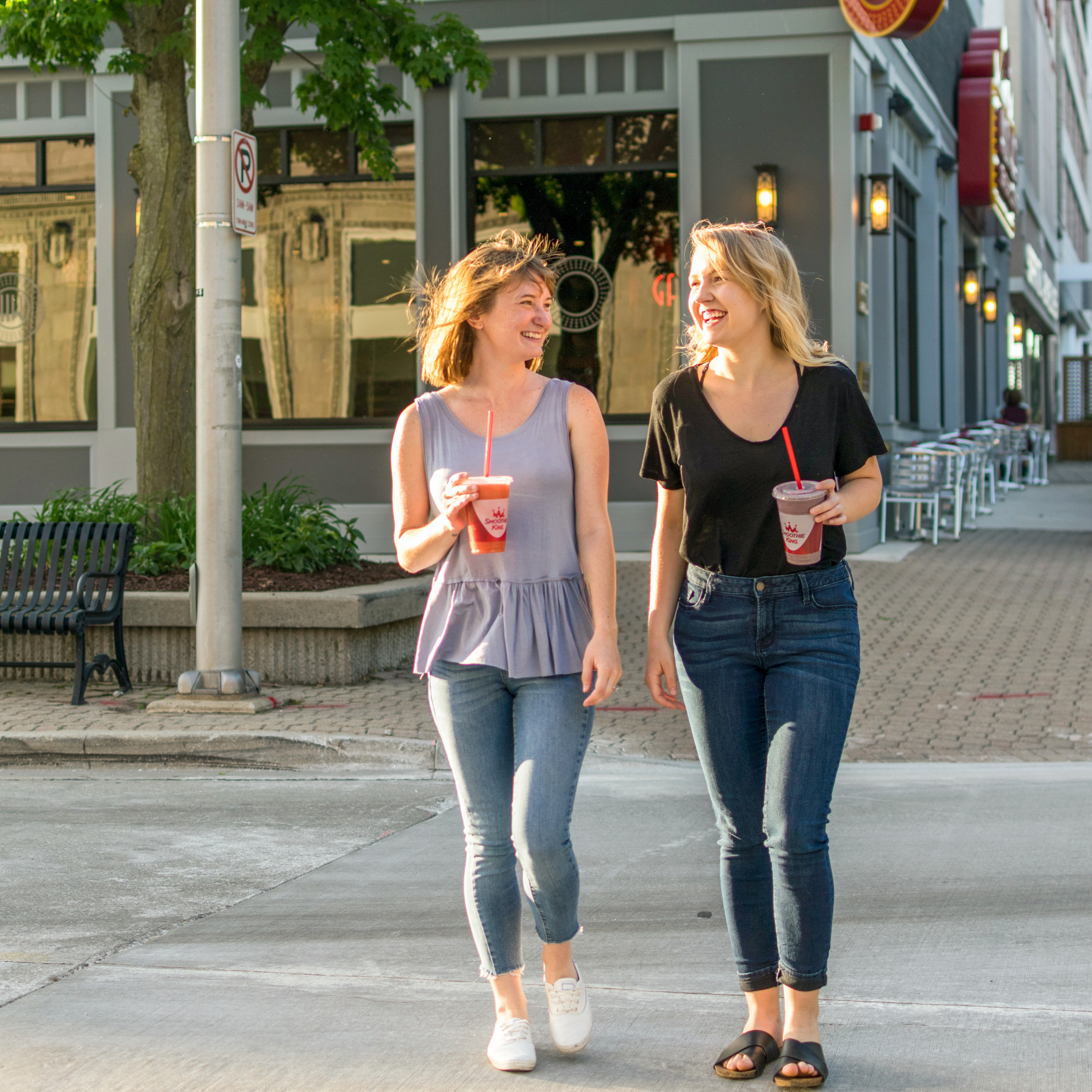 Two women walking in the city with Smoothie King in their hands