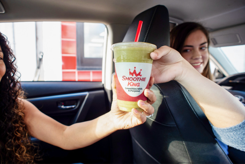 A friend passing a Metabolism Boost® Mango Ginger green smoothie from Smoothie King to her friend in a car