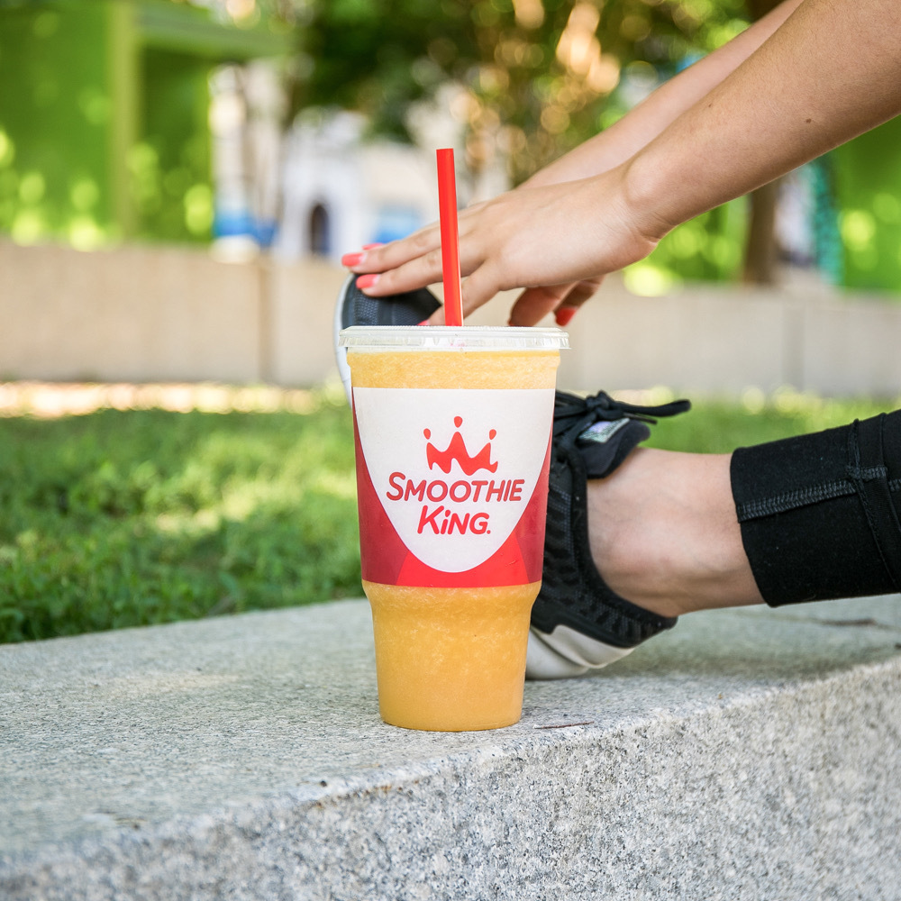 A Smoothie King protein smoothie in front of a woman’s foot stretching