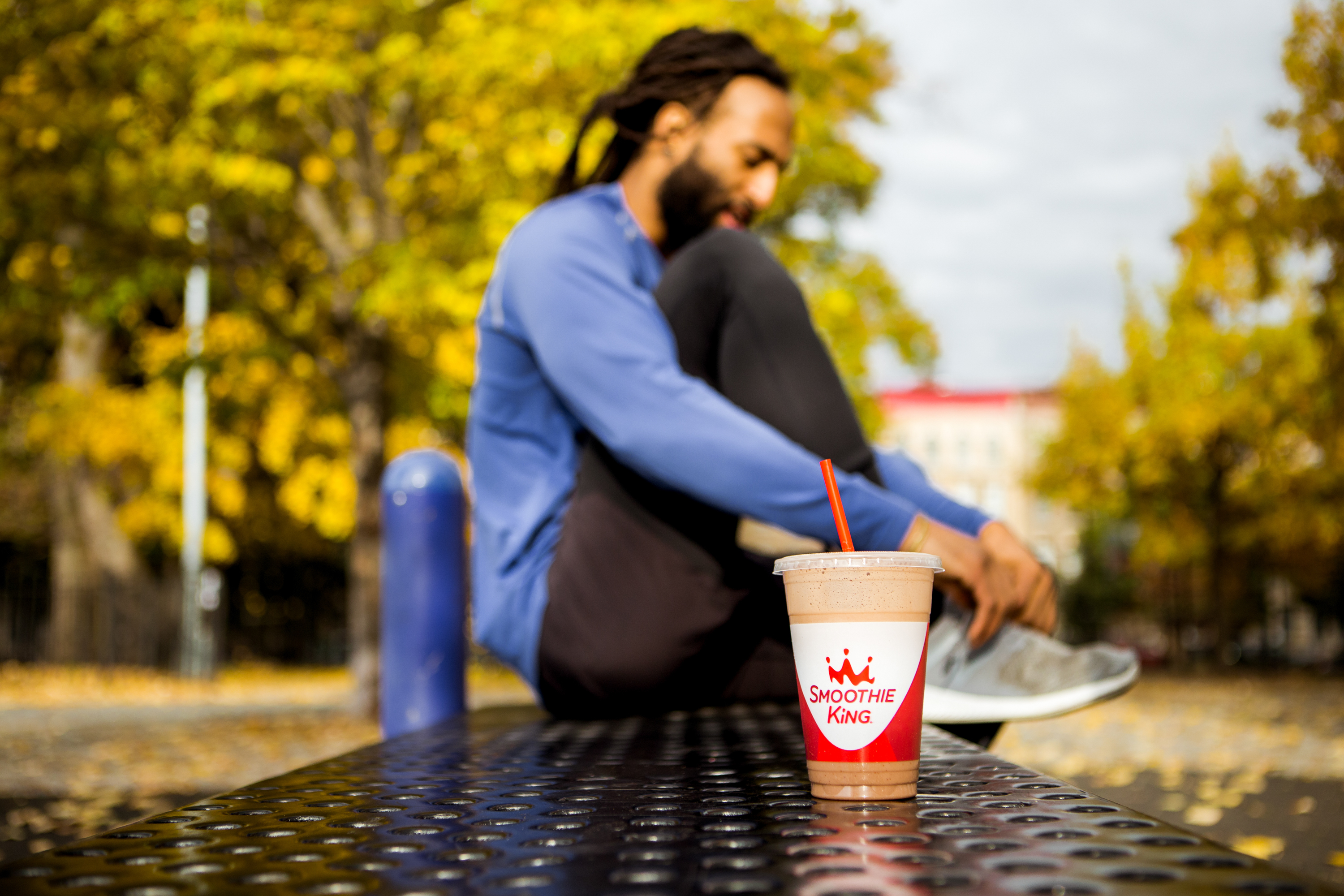 A runner fastens his shoelaces; a smoothie rests in the foreground.