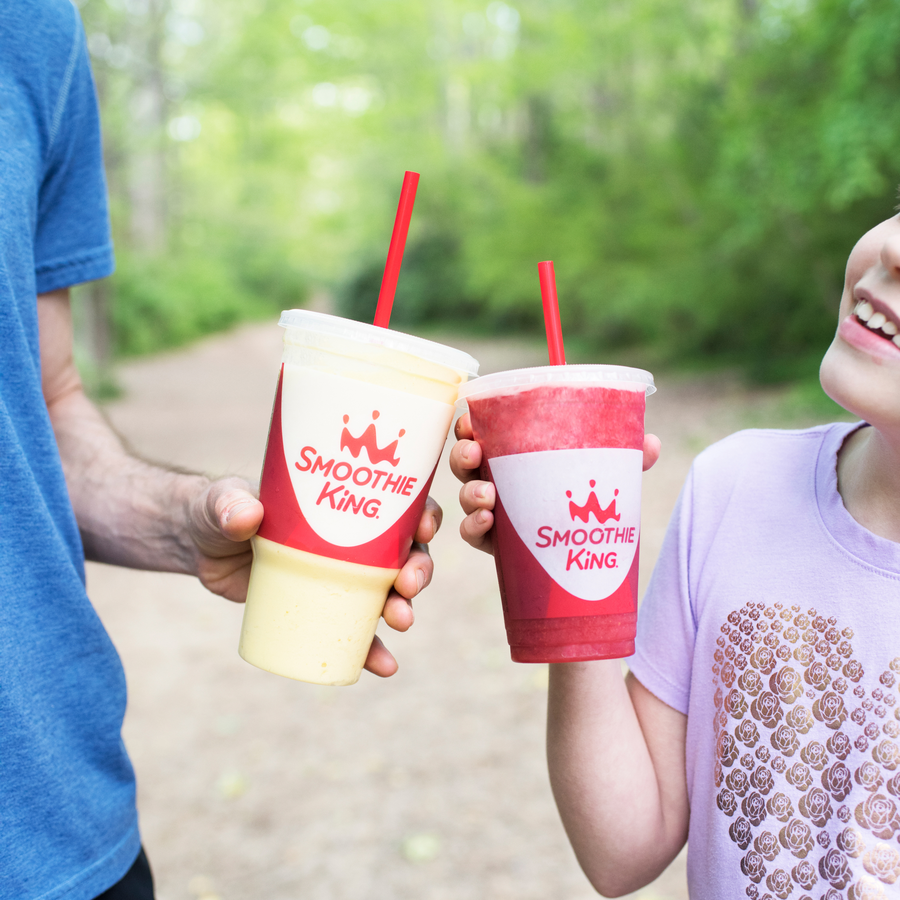 A father and daughter cheer their smoothie cups together while walking outside