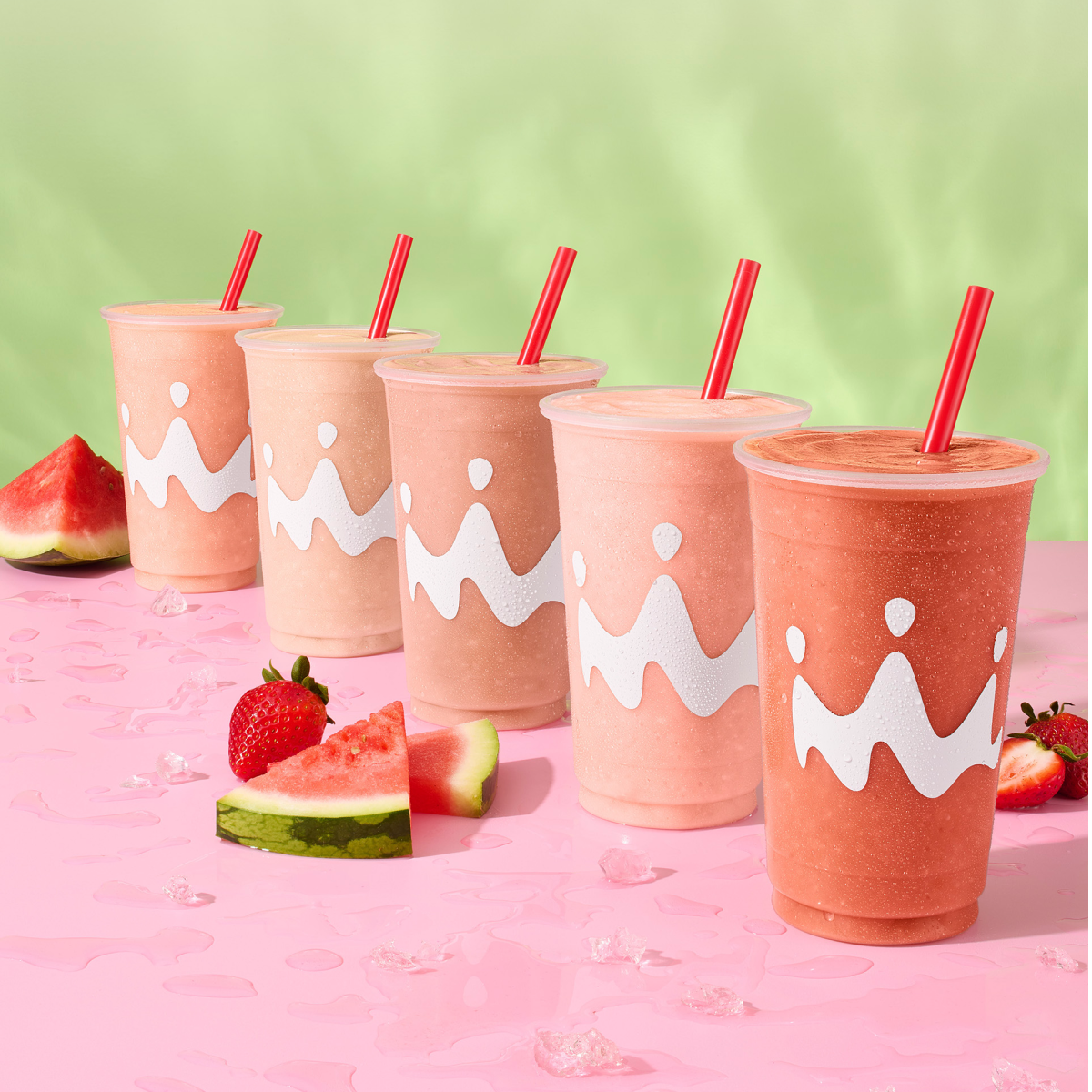 A lineup of all the Smoothie King watermelon smoothies with watermelon slices and strawberries