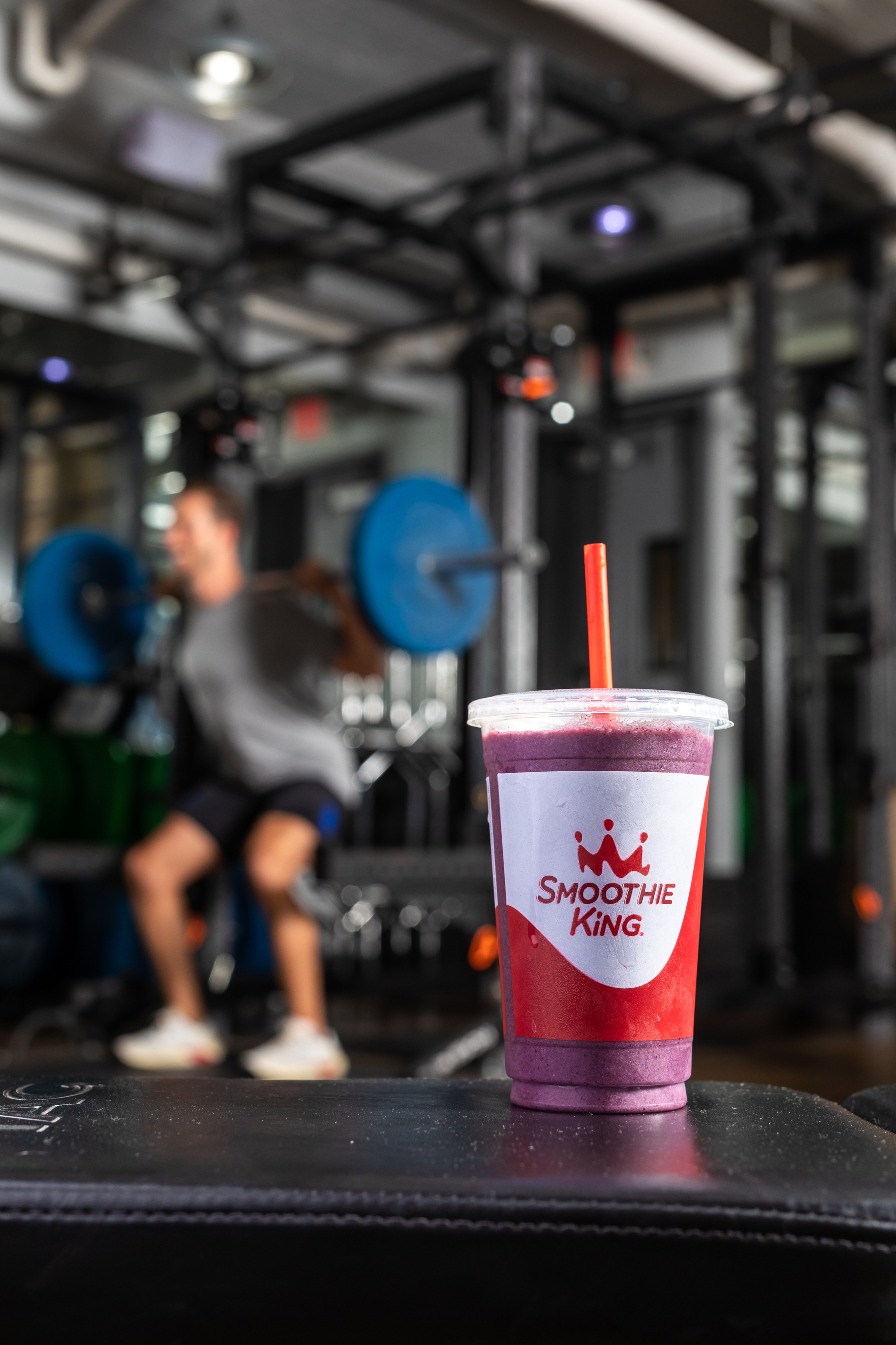 A blueberry raspberry smoothie from Smoothie King in the foreground and a weight lifter squatting in the background