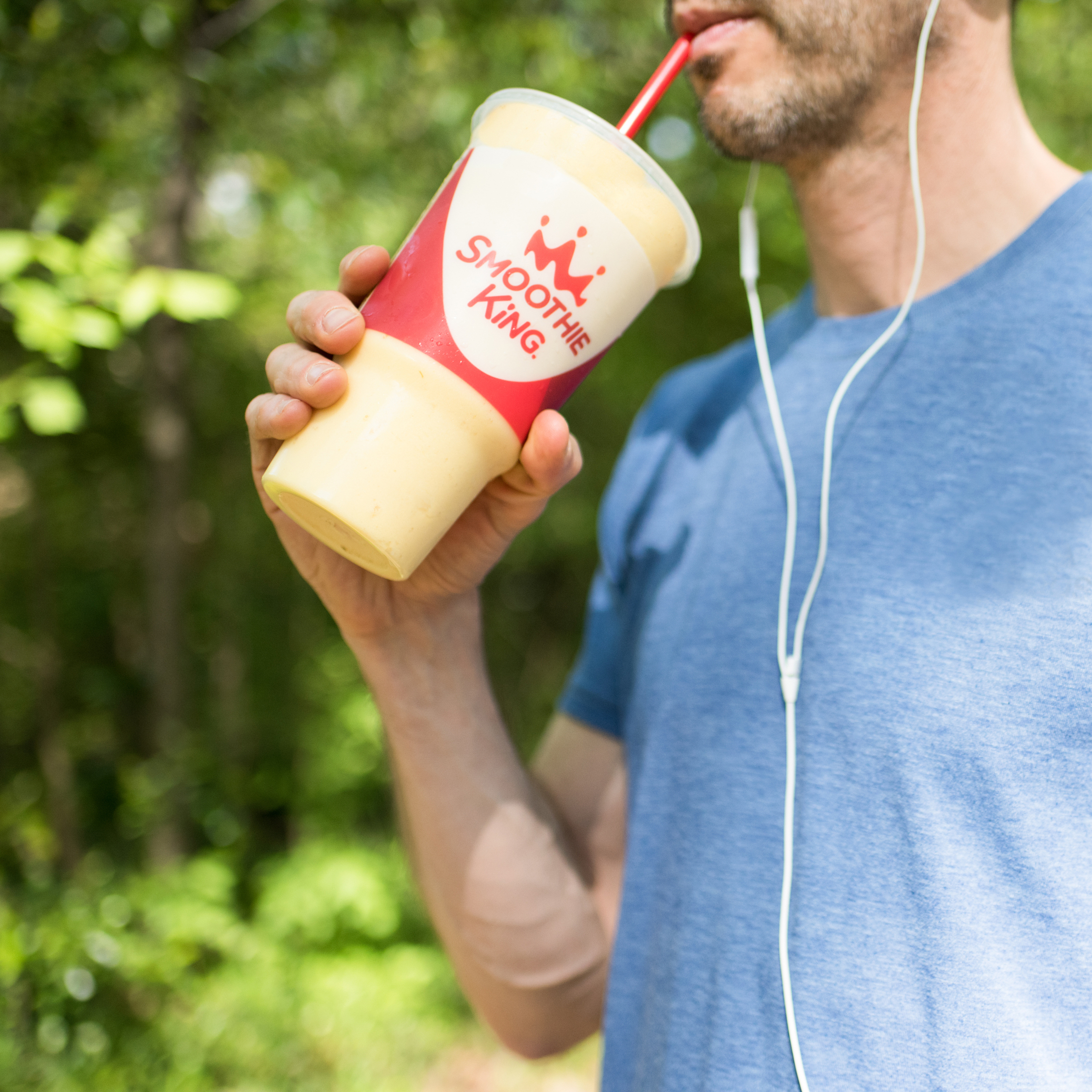 A runner with headphones sipping a pineapple smoothie from Smoothie King