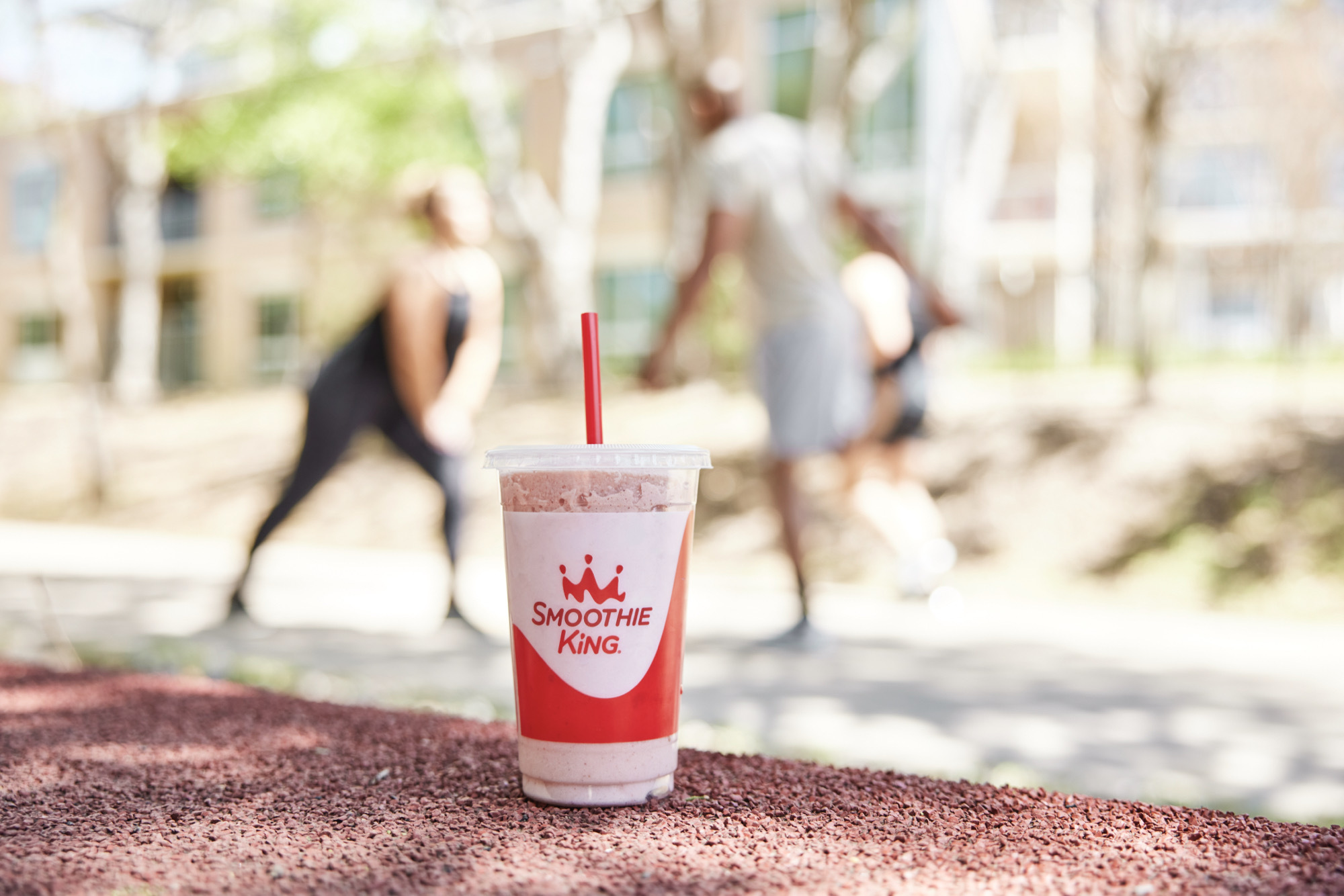 Man and woman stretching for a run with a Smoothie King smoothie cup in the foreground