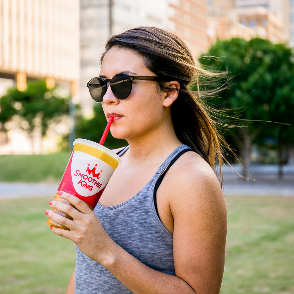 Woman drinking her tasty Smoothie King blend outside featuring unique smoothie ingredients