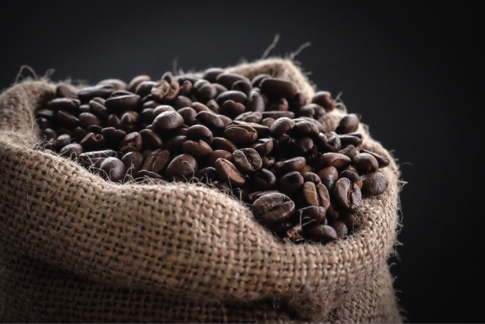 Small burlap sack of brown coffee beans against a black background