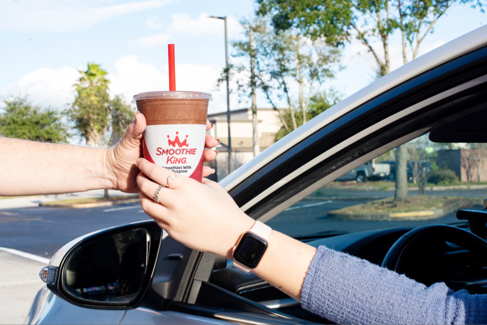 A hand reaches out of a car window to take a coffee smoothie from a drive-thru worker