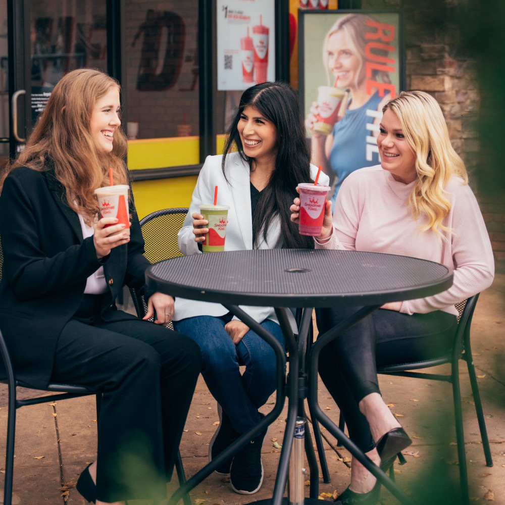 Three female friends sitting outside a Smoothie King enjoying their smoothies