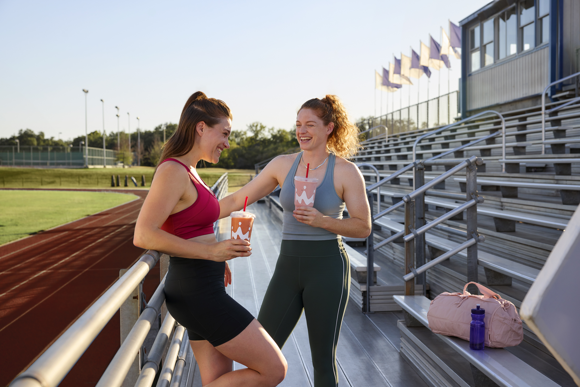 Two women drinking Smoothie King hydration smoothies after a run on a track