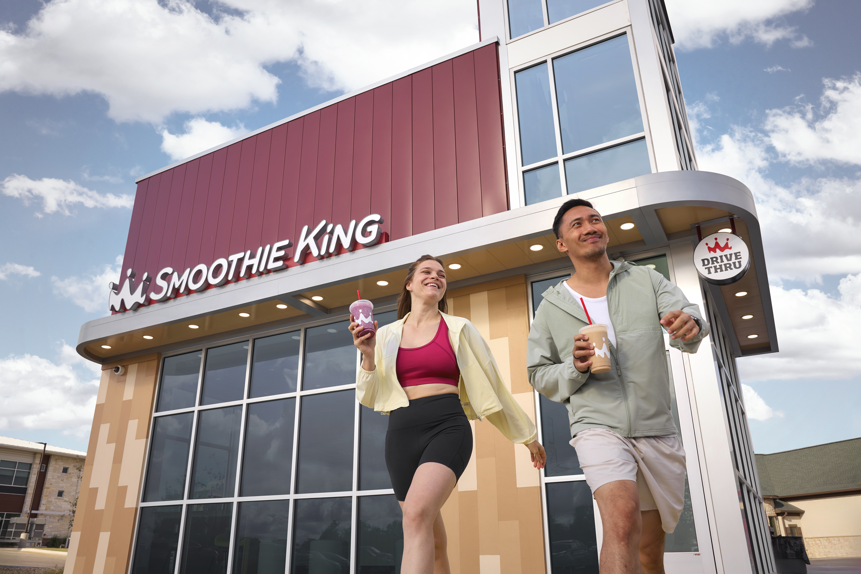 A man and woman happily walk out of a Smoothie King shop with smoothies in hand